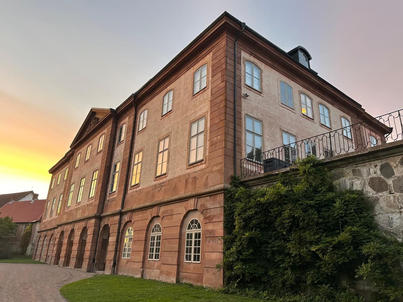 Övedsklosters slott i kvällsljus med sandstensfasaden mot en solnedgång