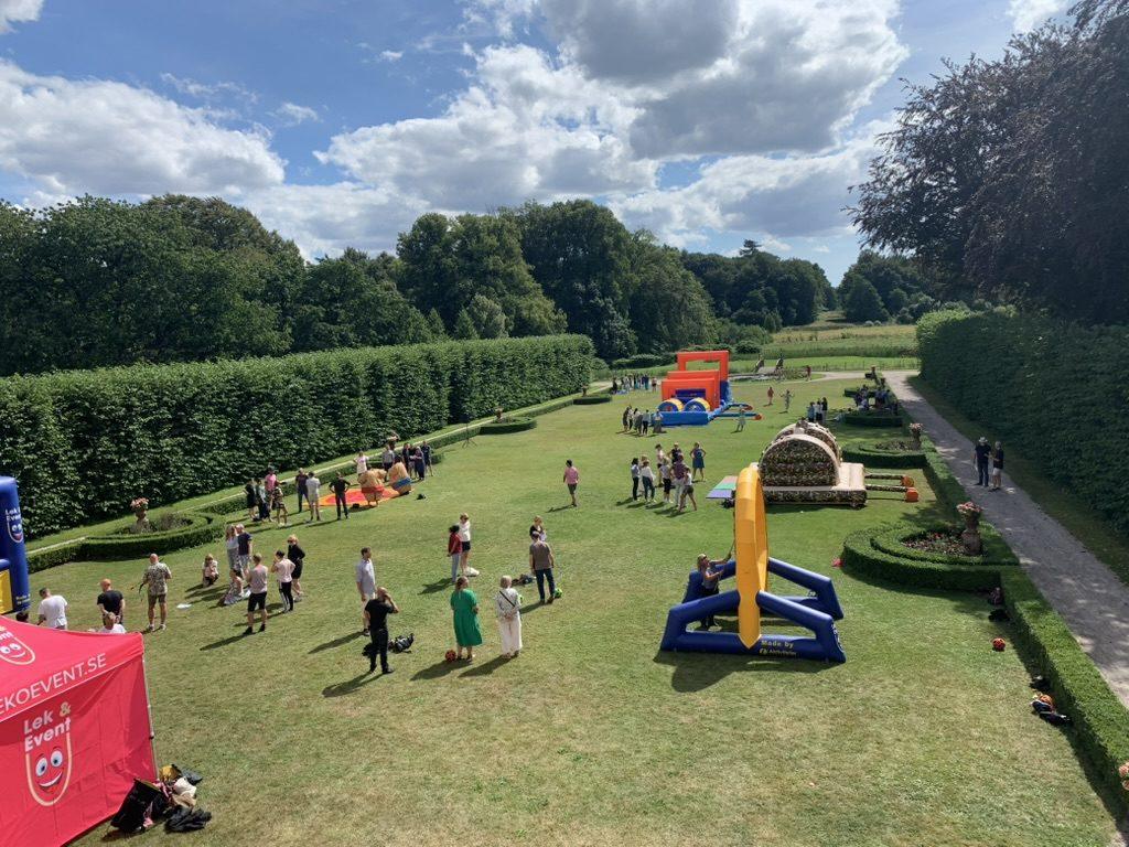 Aktivitetsdag på gräsmattan i Övedsklosters park med uppblåsbara hinderbanor, sumodräkter och ett rött eventtält under blå himmel