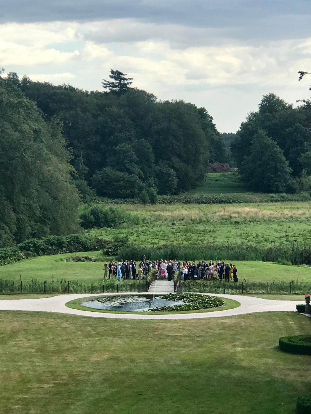 Sällskap samlade vid den runda dammen och träbron i Övedsklosters park