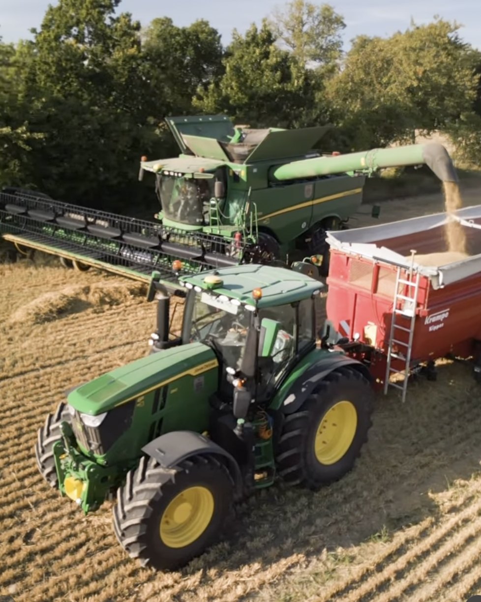 Skördetröska lossar säd ner i en röd spannmålsvagn som drogs av en grön traktor vid skörden