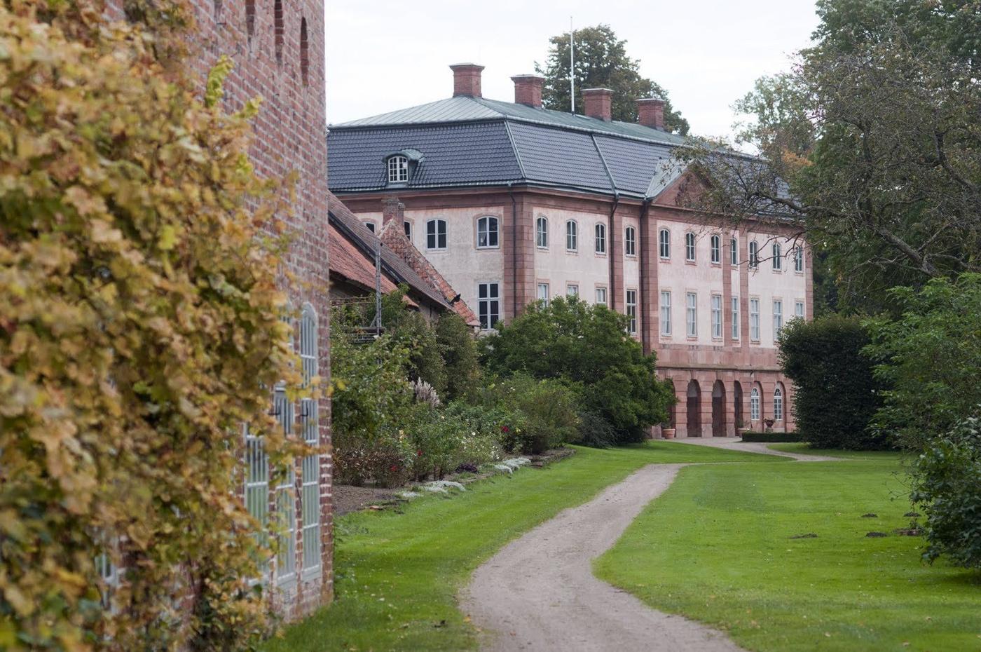Grusgången genom Övedsklosters trädgård med slottet i fonden och tegelbyggnaderna längs gräsmattan